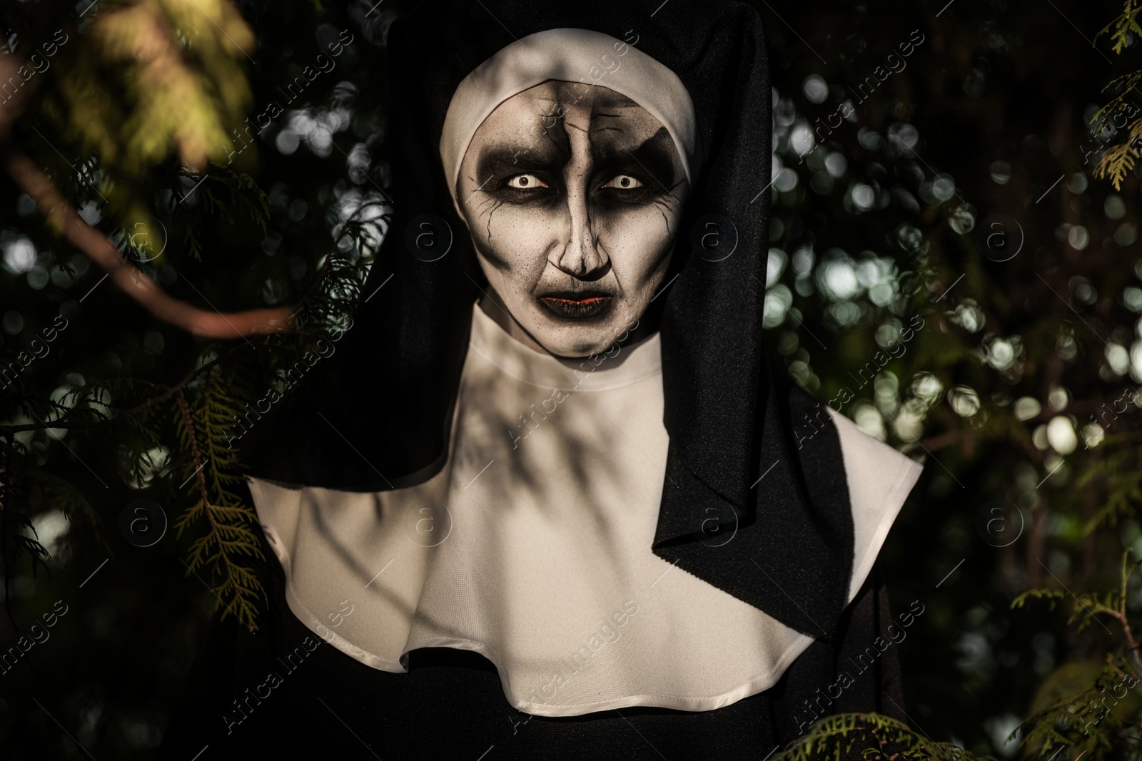 Photo of Portrait of scary devilish nun near tree outdoors. Halloween party look