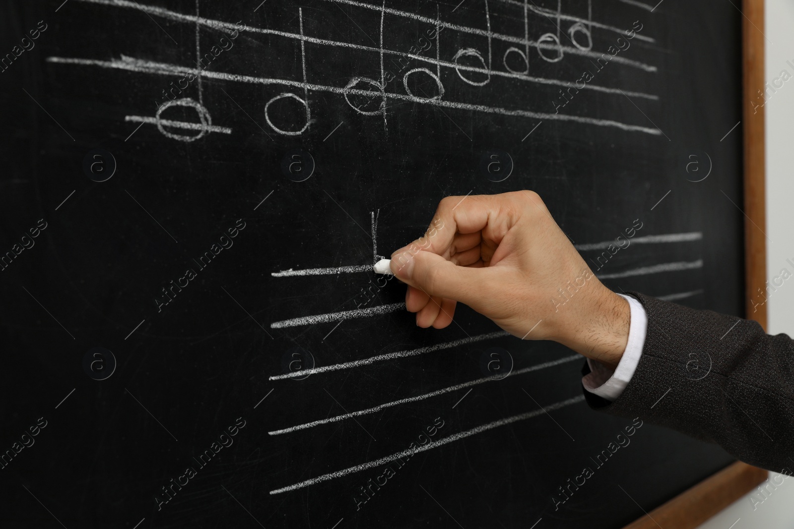 Photo of Teacher writing music notes with chalk on blackboard, closeup