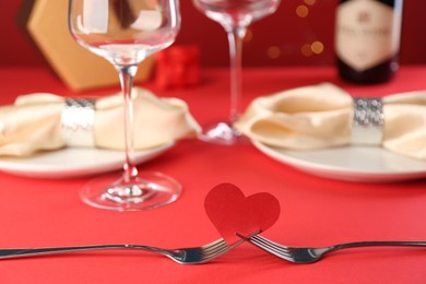 Photo of Joined forks with paper heart on red table, closeup. Romantic dinner