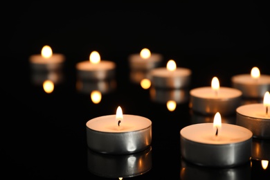 Photo of Many burning candles on black table in darkness