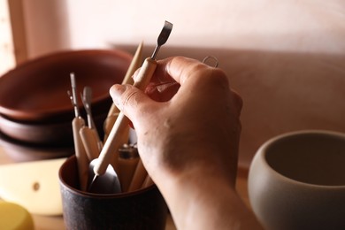 Photo of Woman taking clay crafting tool from cup in workshop, closeup