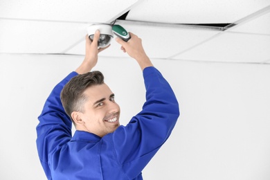 Technician installing CCTV camera on ceiling indoors