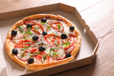 Photo of Cardboard box with tasty pizza on wooden table