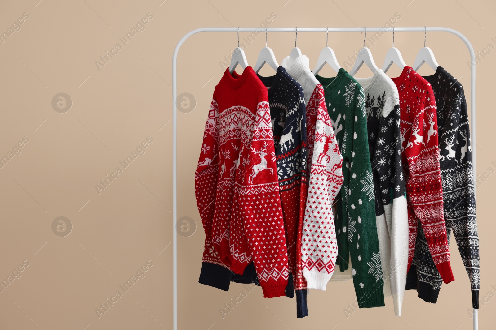 Photo of Rack with different Christmas sweaters on beige background, space for text