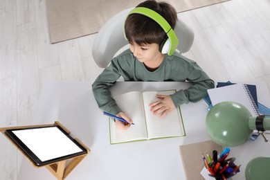 Photo of Cute little boy with modern tablet studying online at home, above view. E-learning
