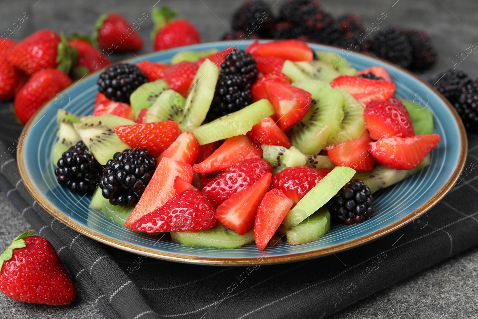 Photo of Plate of delicious fresh fruit salad on grey textured table, closeup