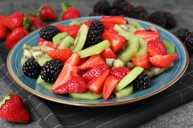 Photo of Plate of delicious fresh fruit salad on grey textured table, closeup