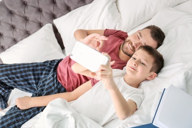 Photo of Little boy taking selfie with his dad in bedroom