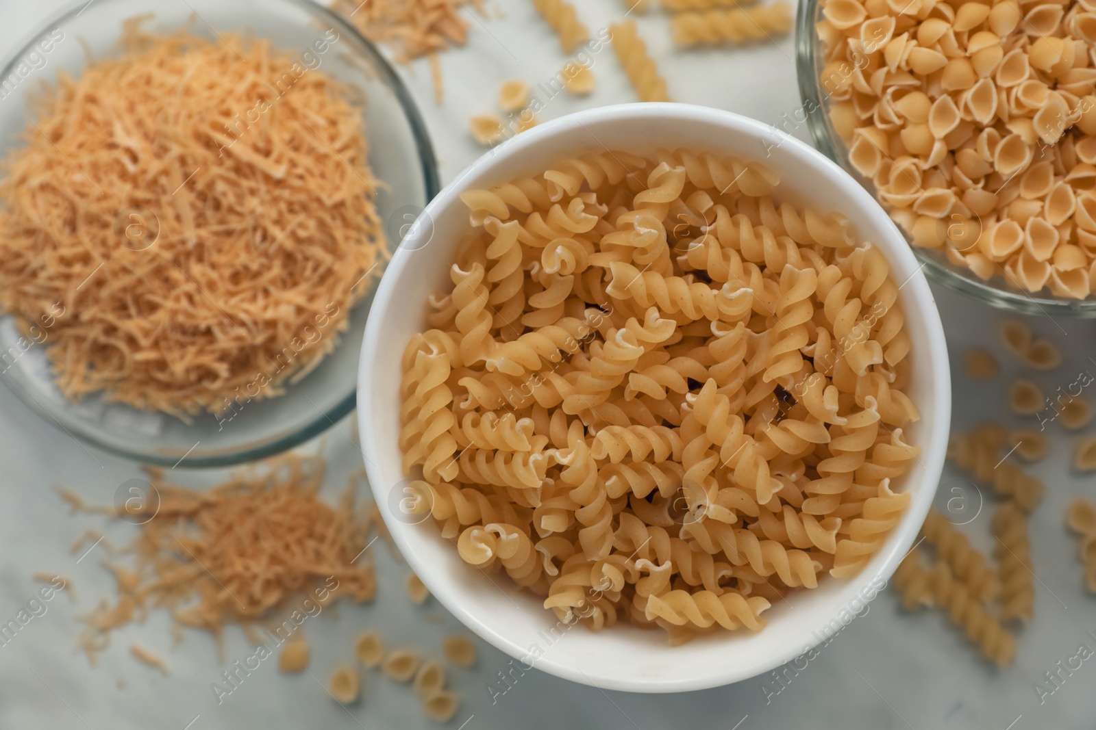 Photo of Different types of pasta on white marble table, flat lay