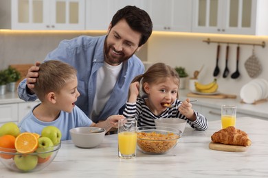 Photo of Father and his little children having breakfast at table in kitchen