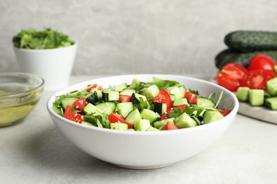 Photo of Delicious salad with cucumbers, tomatoes and sesame seeds in bowl on light table