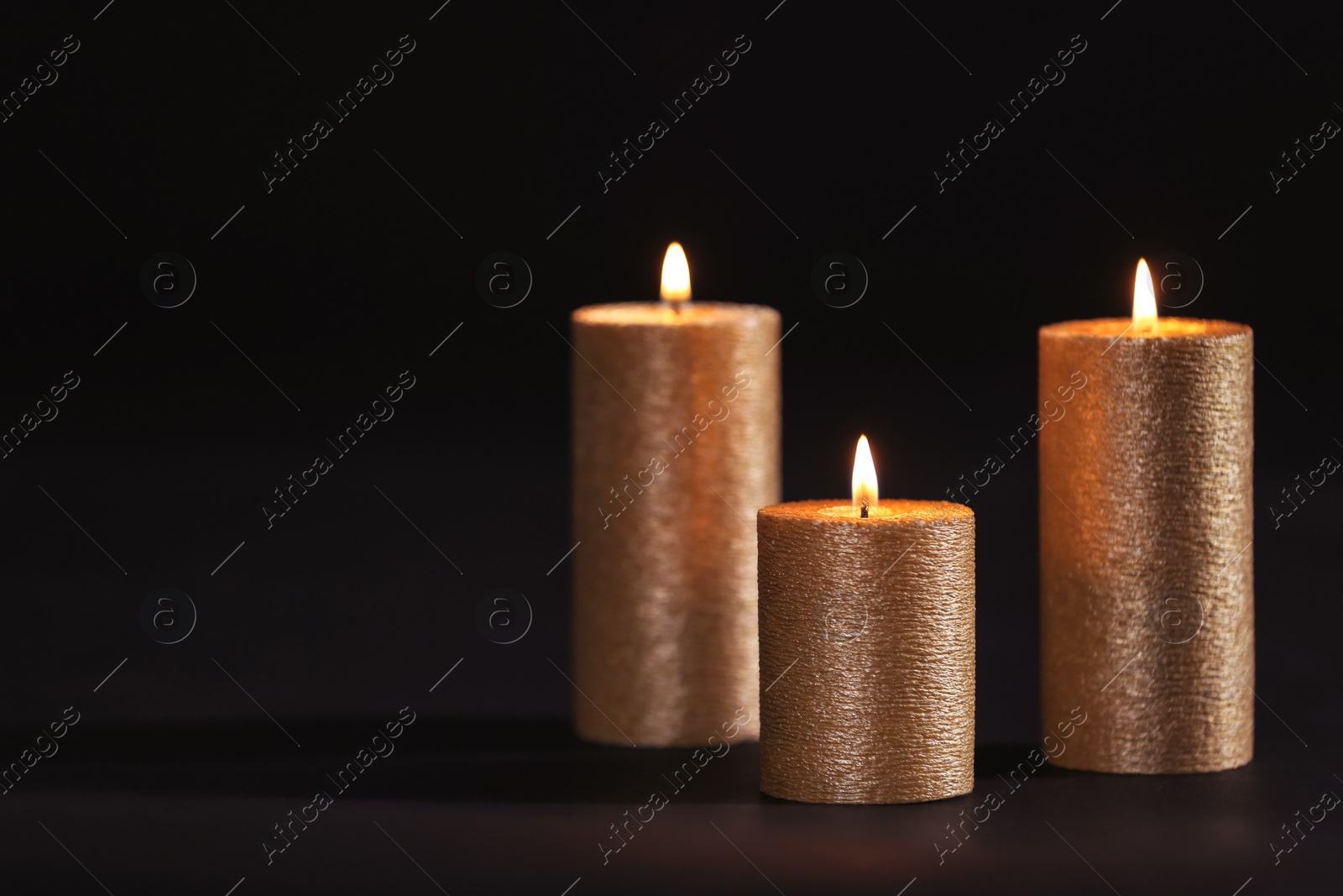 Photo of Burning gold candles on black background, space for text