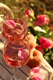 Glasses of delicious rose wine with petals on white picnic blanket outside