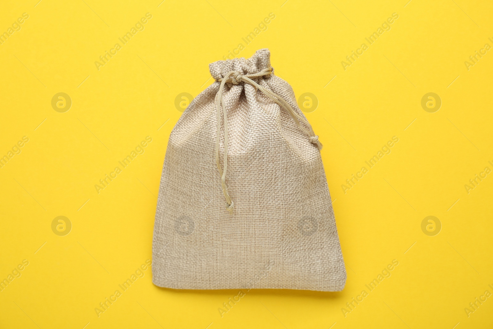 Photo of Tied burlap bag on yellow background, top view