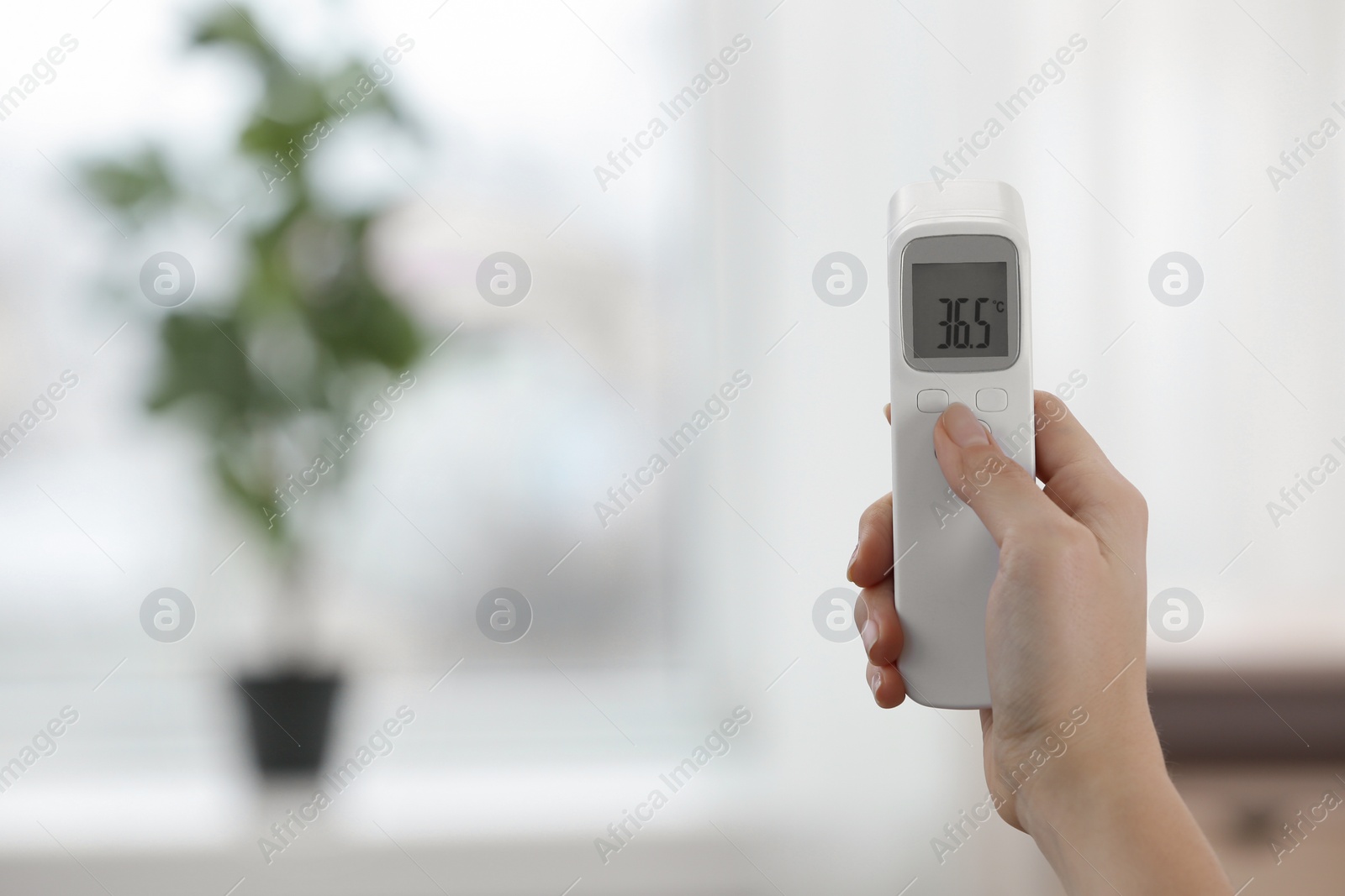 Photo of Closeup view of woman with infrared thermometer on blurred background, space for text. Checking temperature during Covid-19 pandemic