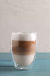 Photo of Glass of delicious layered coffee on turquoise wooden table against white background, space for text