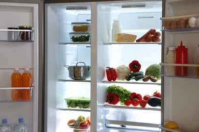 Photo of Open refrigerator full of different products indoors