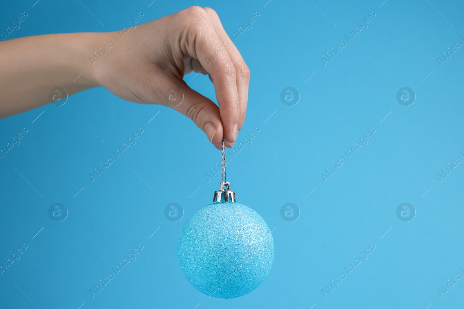 Photo of Woman holding glitter Christmas ball on light blue background, closeup. Space for text