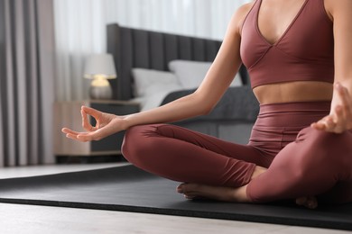 Woman practicing Padmasana on yoga mat at home, closeup. Lotus pose