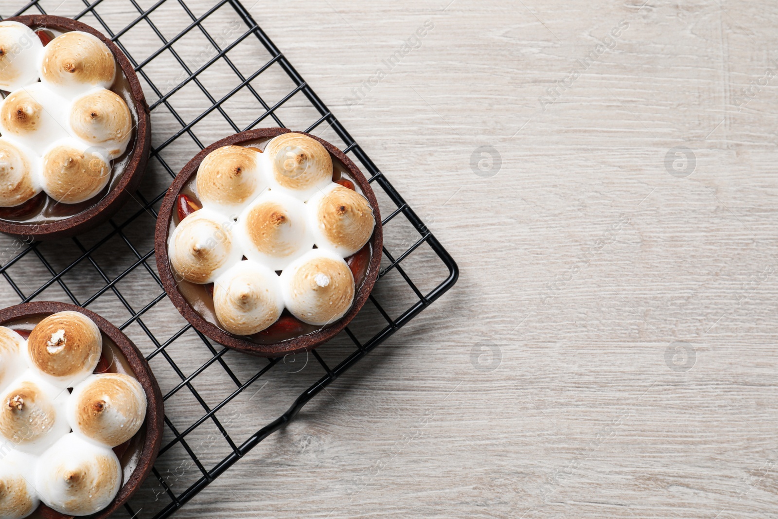 Photo of Delicious salted caramel meringue tarts on light wooden table, flat lay. Space for text