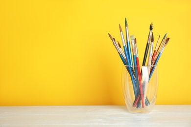 Photo of Glass with paint brushes on table against color background. Space for text