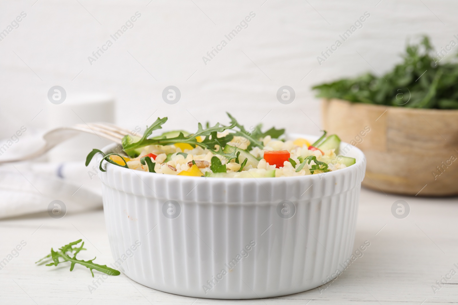 Photo of Cooked bulgur with vegetables in bowl on white wooden table, closeup