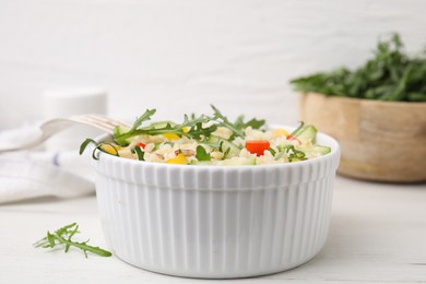 Cooked bulgur with vegetables in bowl on white wooden table, closeup