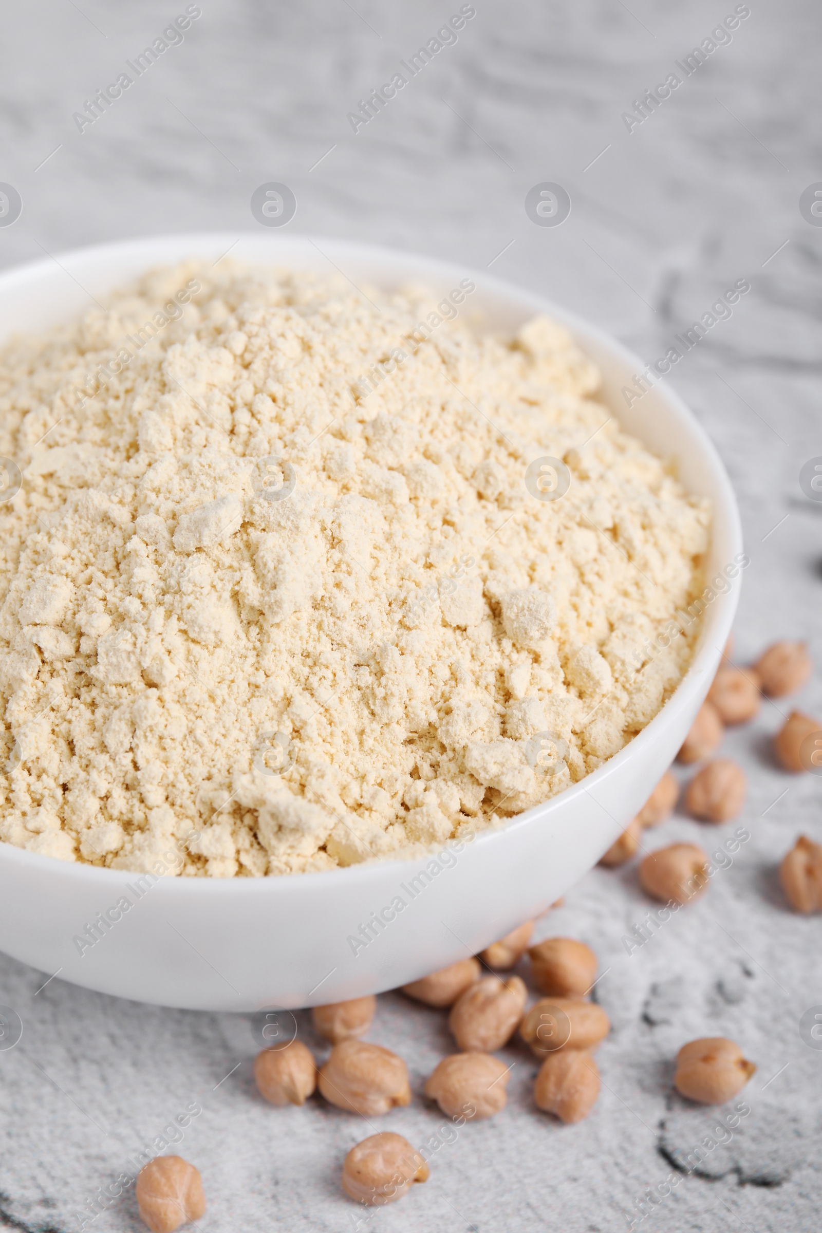 Photo of Chickpea flour in bowl and seeds on light grey textured table, closeup