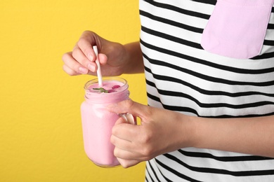 Photo of Woman holding mason jar with delicious raspberry smoothie on yellow background, closeup