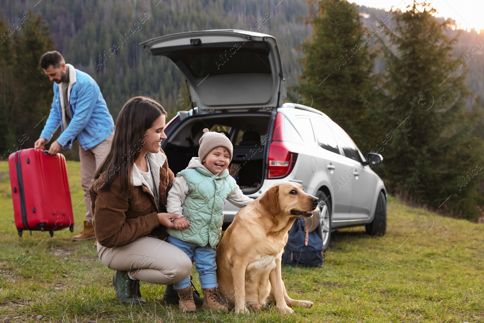 Photo of Mother with her daughter, dog and man near car in mountains. Family traveling with pet