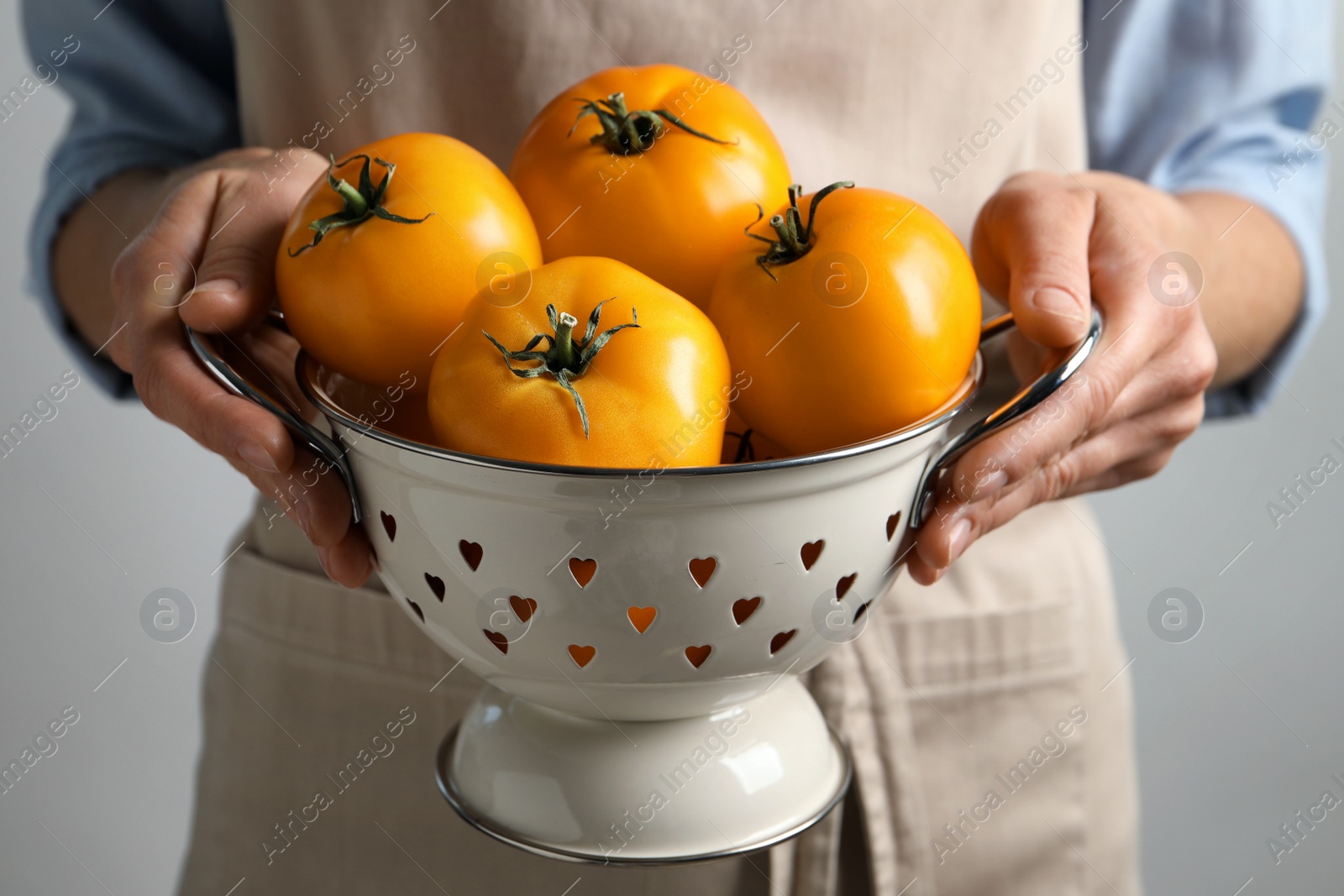 Photo of Woman holding colander with fresh ripe yellow tomatoes, closeup