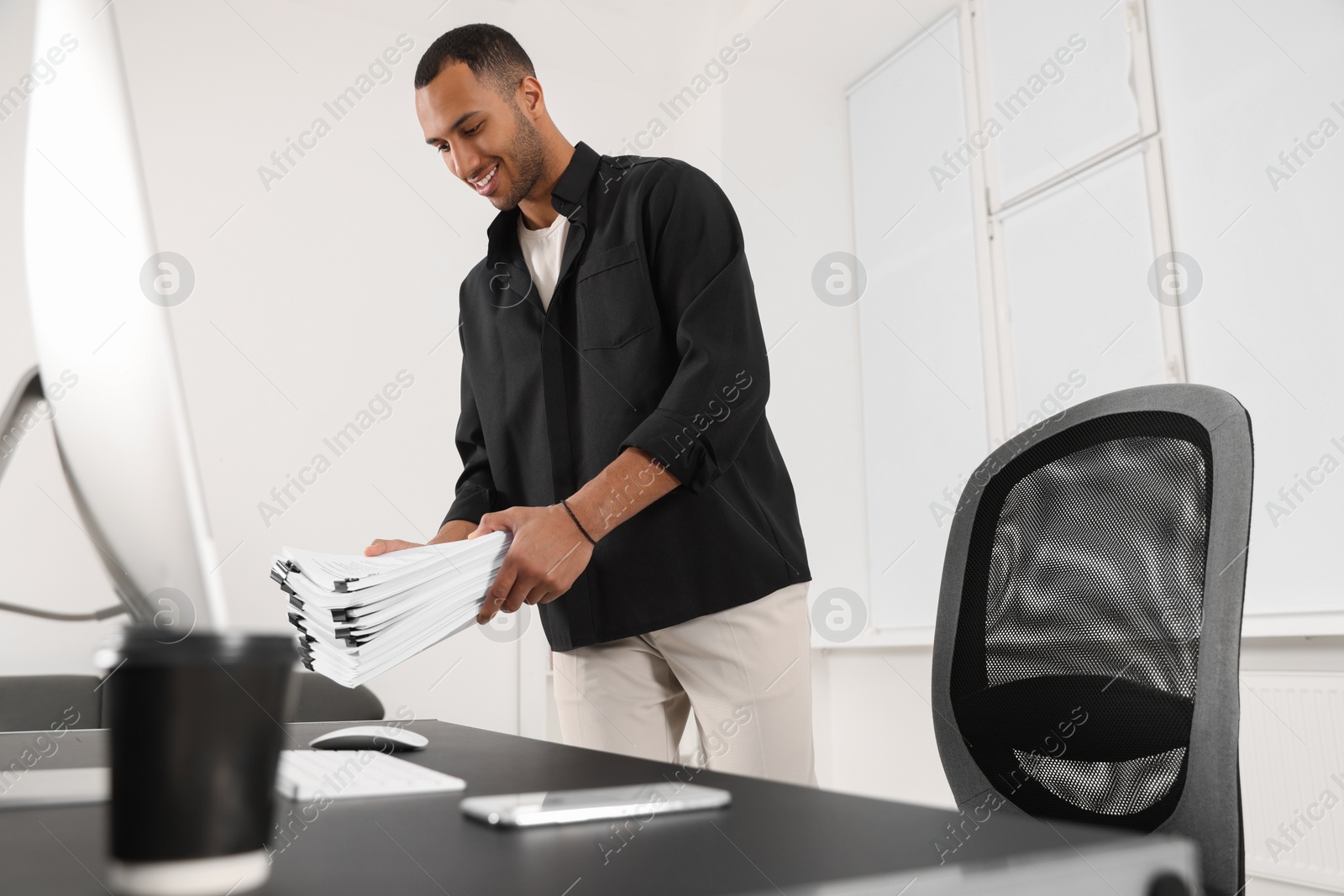 Photo of Happy man with documents near table in office
