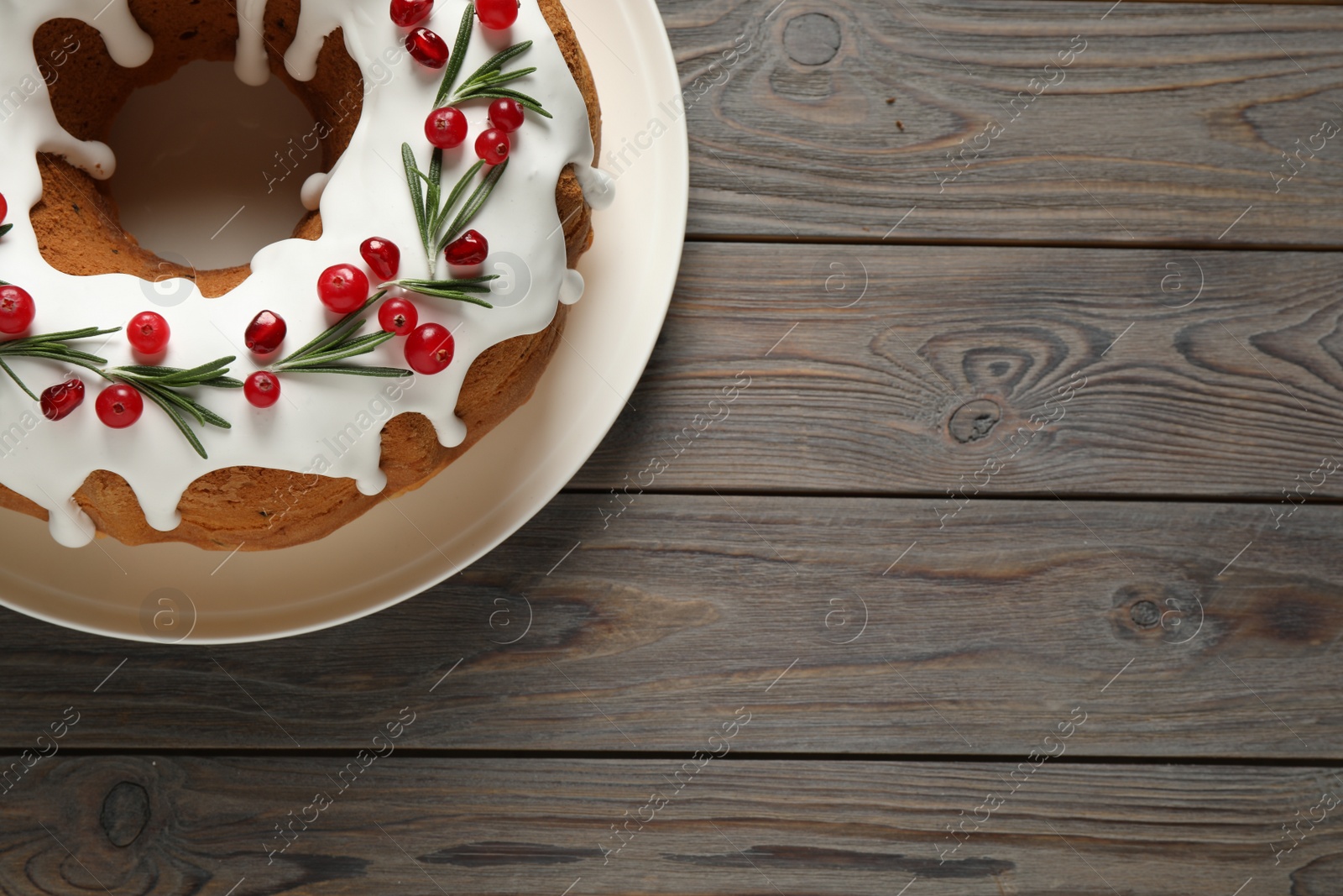 Photo of Traditional Christmas cake decorated with glaze, pomegranate seeds, cranberries and rosemary on wooden table, top view. Space for text