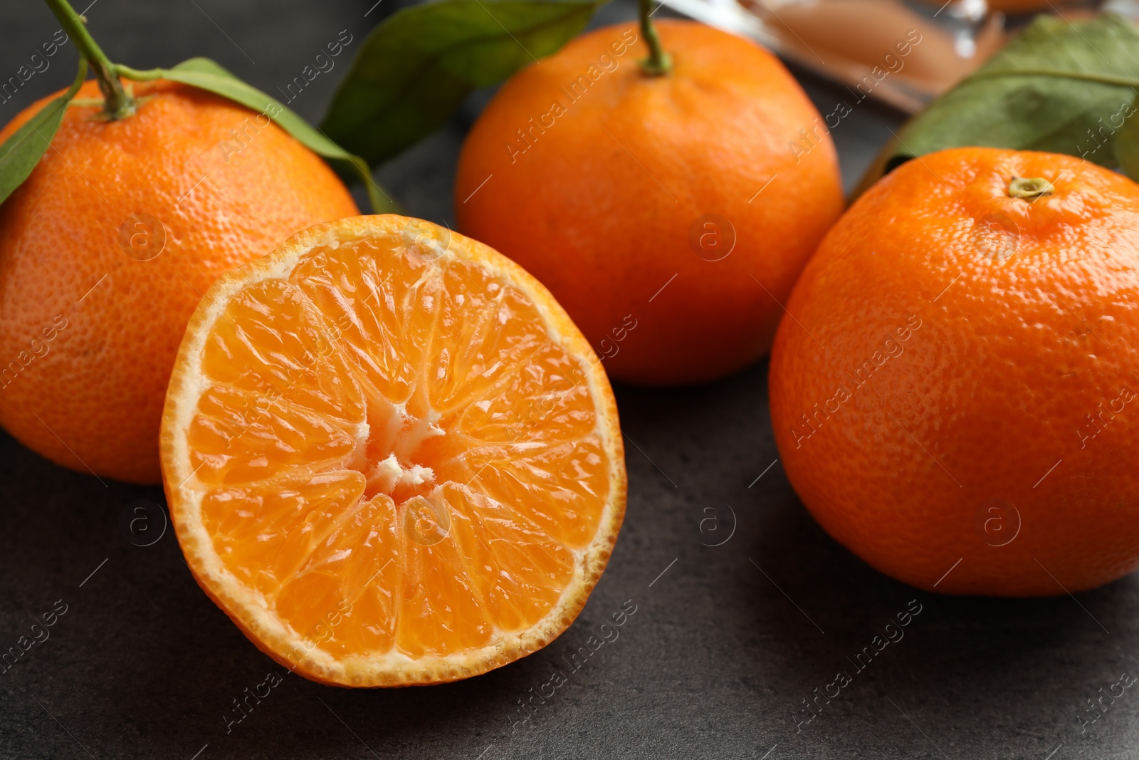 Photo of Fresh ripe tangerines and green leaves on grey table, closeup