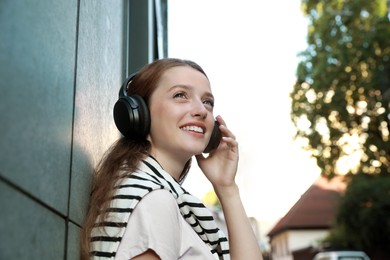 Photo of Smiling woman in headphones listening to music near building outdoors