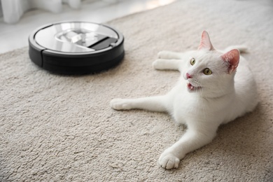 Photo of Modern robotic vacuum cleaner and cute cat on floor indoors