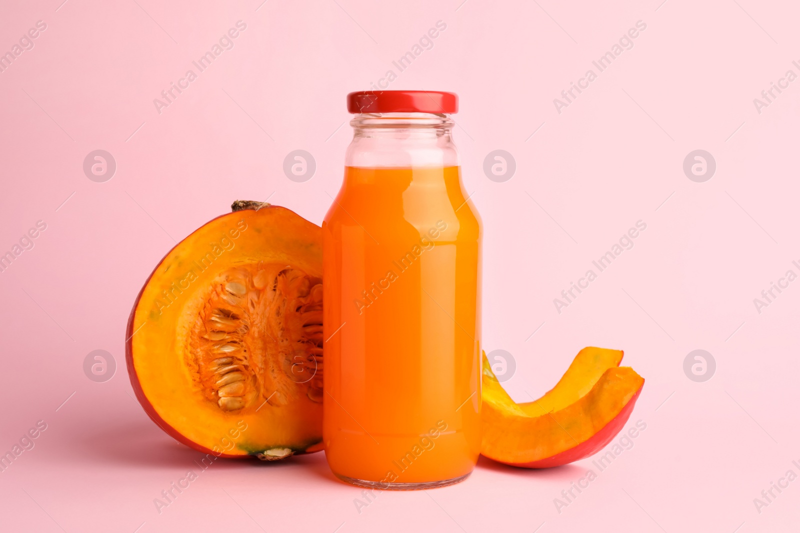 Photo of Tasty pumpkin juice in glass bottle and cut pumpkin on pink background