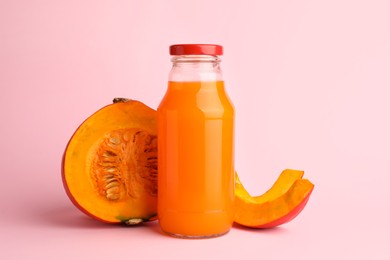 Tasty pumpkin juice in glass bottle and cut pumpkin on pink background