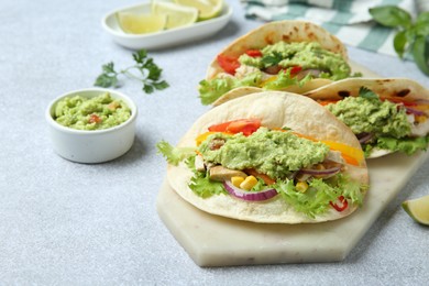 Photo of Delicious tacos with guacamole, meat and vegetables on light grey table