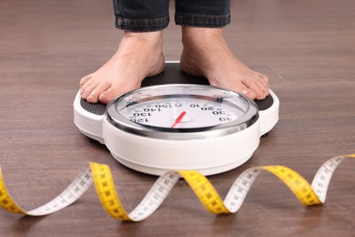 Woman using scales on floor near measuring tape, closeup. Overweight problem