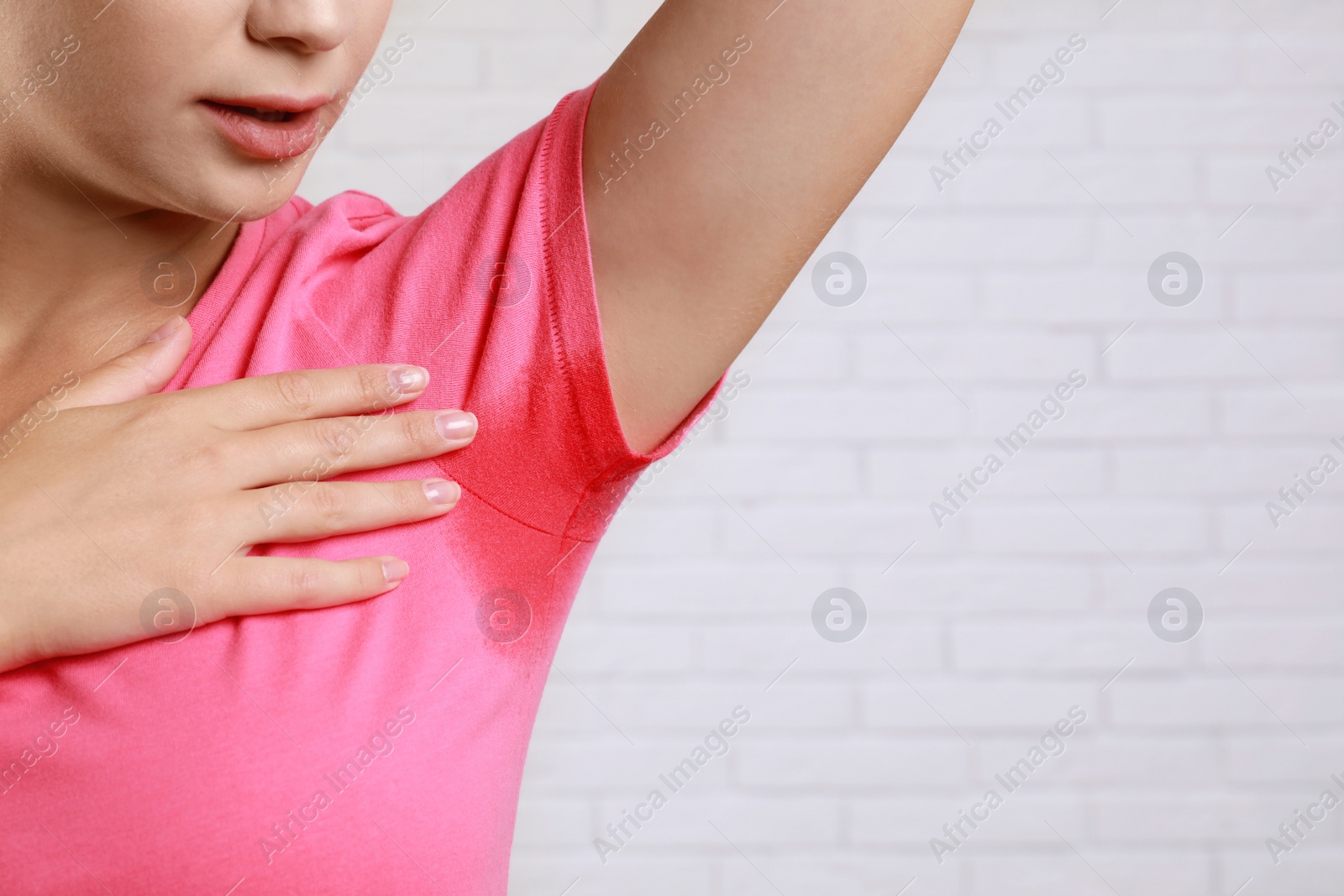 Photo of Young woman with sweat stain on her clothes against brick wall, closeup. Using deodorant