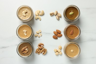 Photo of Tasty nut butters in jars and raw nuts on white marble table, flat lay