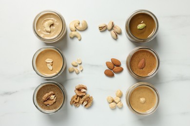 Tasty nut butters in jars and raw nuts on white marble table, flat lay