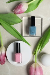 Flat lay composition with bright nail polishes in bottles and tulip flowers on light textured table