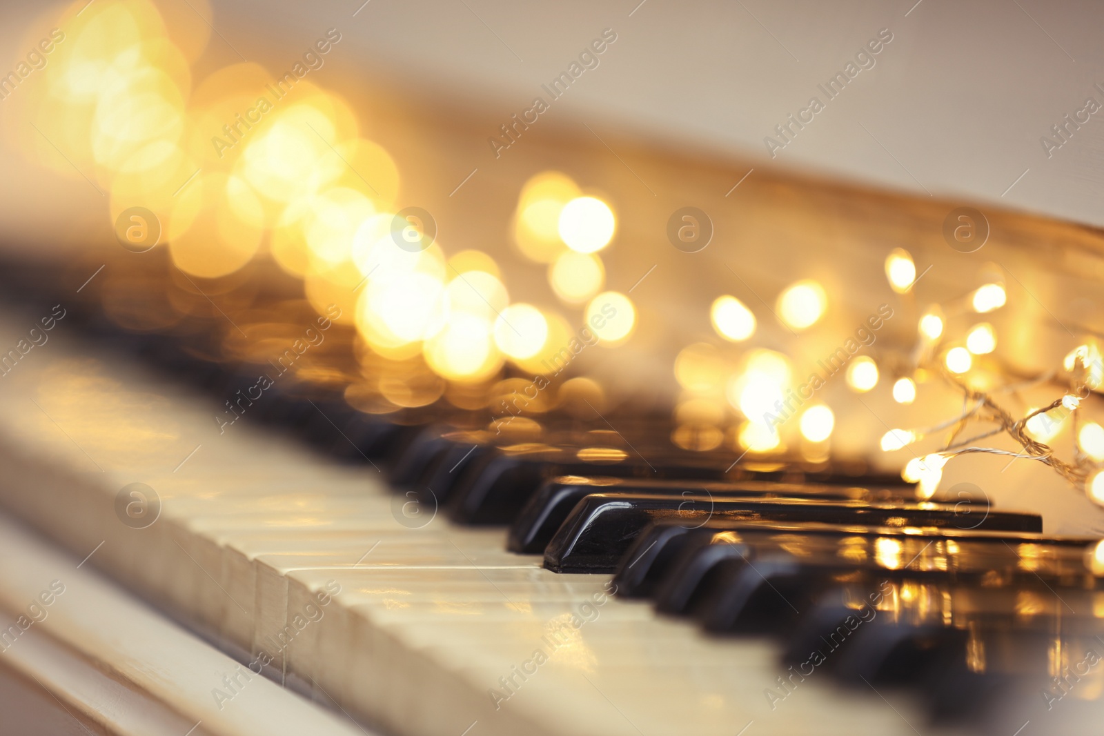 Photo of Glowing fairy lights on piano keys, closeup. Christmas music