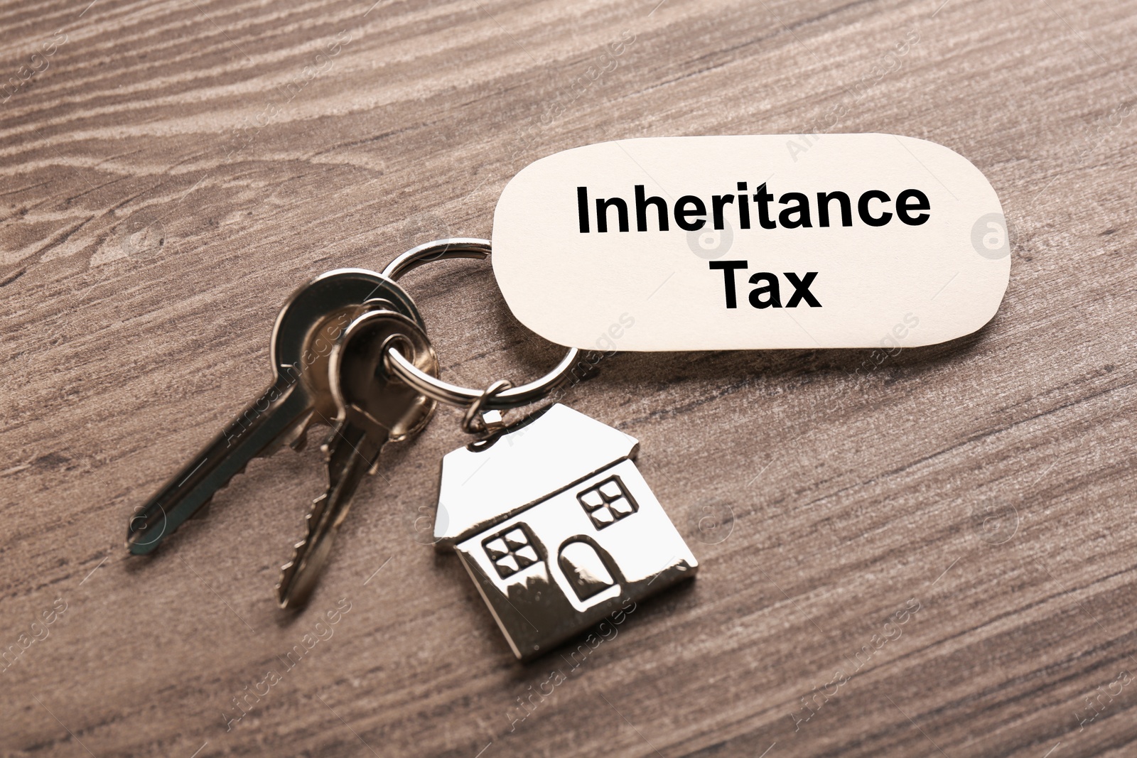 Photo of Inheritance Tax. Card and keys with key chain in shape of house on wooden table, closeup