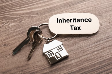 Photo of Inheritance Tax. Card and keys with key chain in shape of house on wooden table, closeup