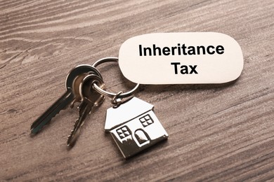 Inheritance Tax. Card and keys with key chain in shape of house on wooden table, closeup