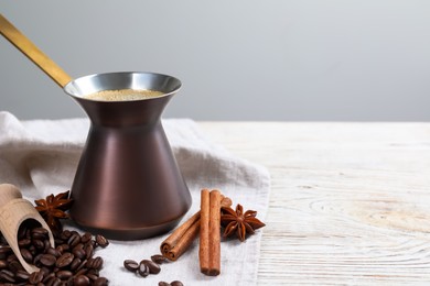 Hot turkish coffee pot, beans and spices on white wooden table, space for text