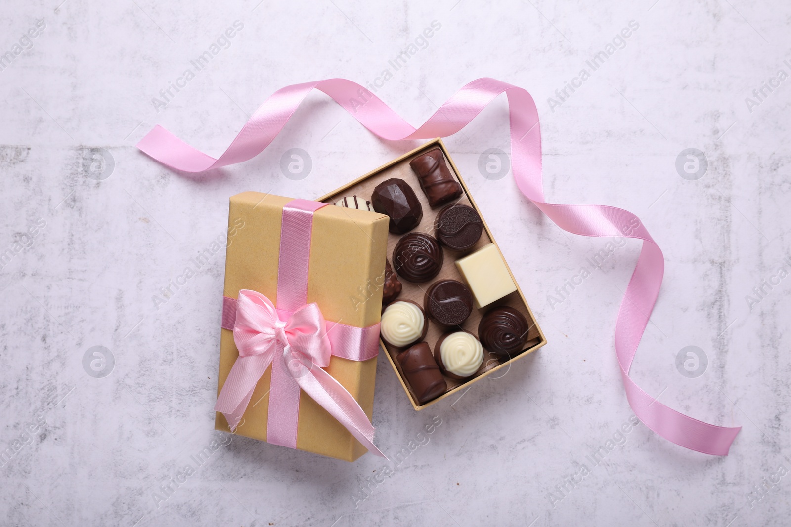 Photo of Open box with delicious chocolate candies and pink ribbon on white table, top view